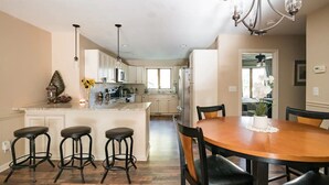 A modern kitchen with a central island, bar stools, and a dining table with chairs. - Mountain Cabin in Town (Wake Forest)