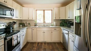 A kitchen with white cabinets, a stainless steel refrigerator, a microwave, and a sink. - Mountain Cabin in Town (Wake Forest)