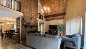 A spacious living room with a large gray sofa, a fireplace, a television, and a dining area with a wooden table and chairs. - Mountain Cabin in Town (Wake Forest)