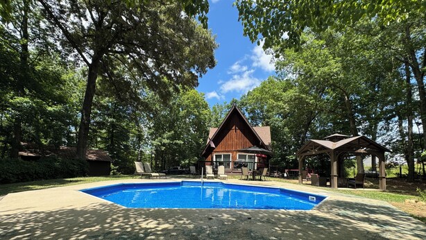 A swimming pool surrounded by trees, a wooden building, and a gazebo. - Mountain Cabin in Town (Wake Forest)