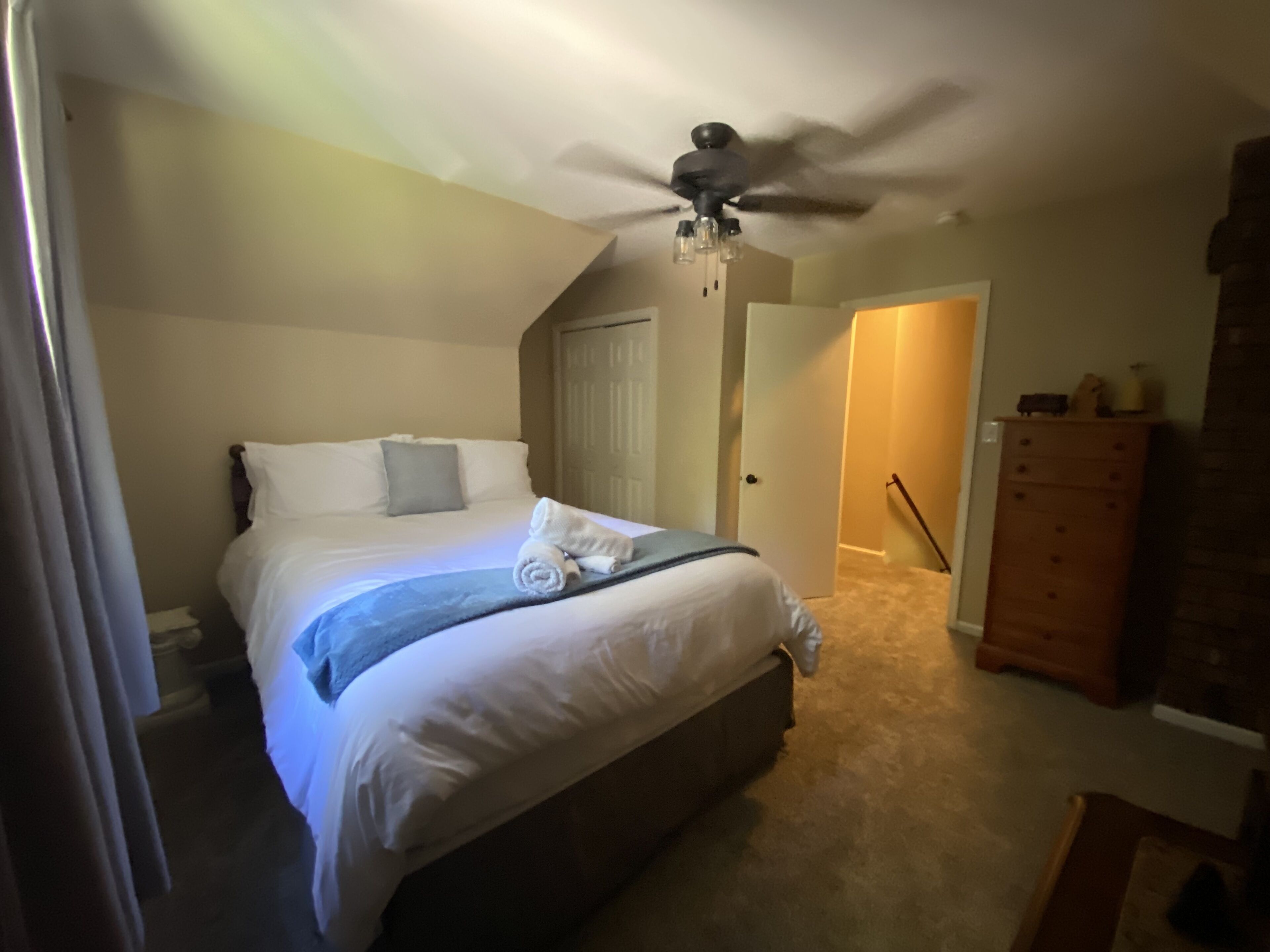 A bedroom with a bed, a ceiling fan, a dresser, and a door leading to another room.