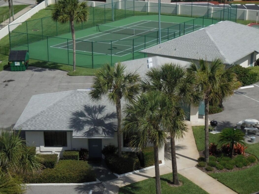 Un quartier résidentiel doté d’un court de tennis, de palmiers et d’une maison à toit en pente.