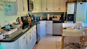 A kitchen with white cabinets, a black countertop, and a dining area with a table and chairs. - ERROL BY THE SEA, 2bdrm 2 bath FIRST FLOOR (New Smyrna Beach)