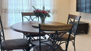 Een eetruimte met een ronde tafel, vier stoelen, een vaas met bloemen en een plafondventilator.
