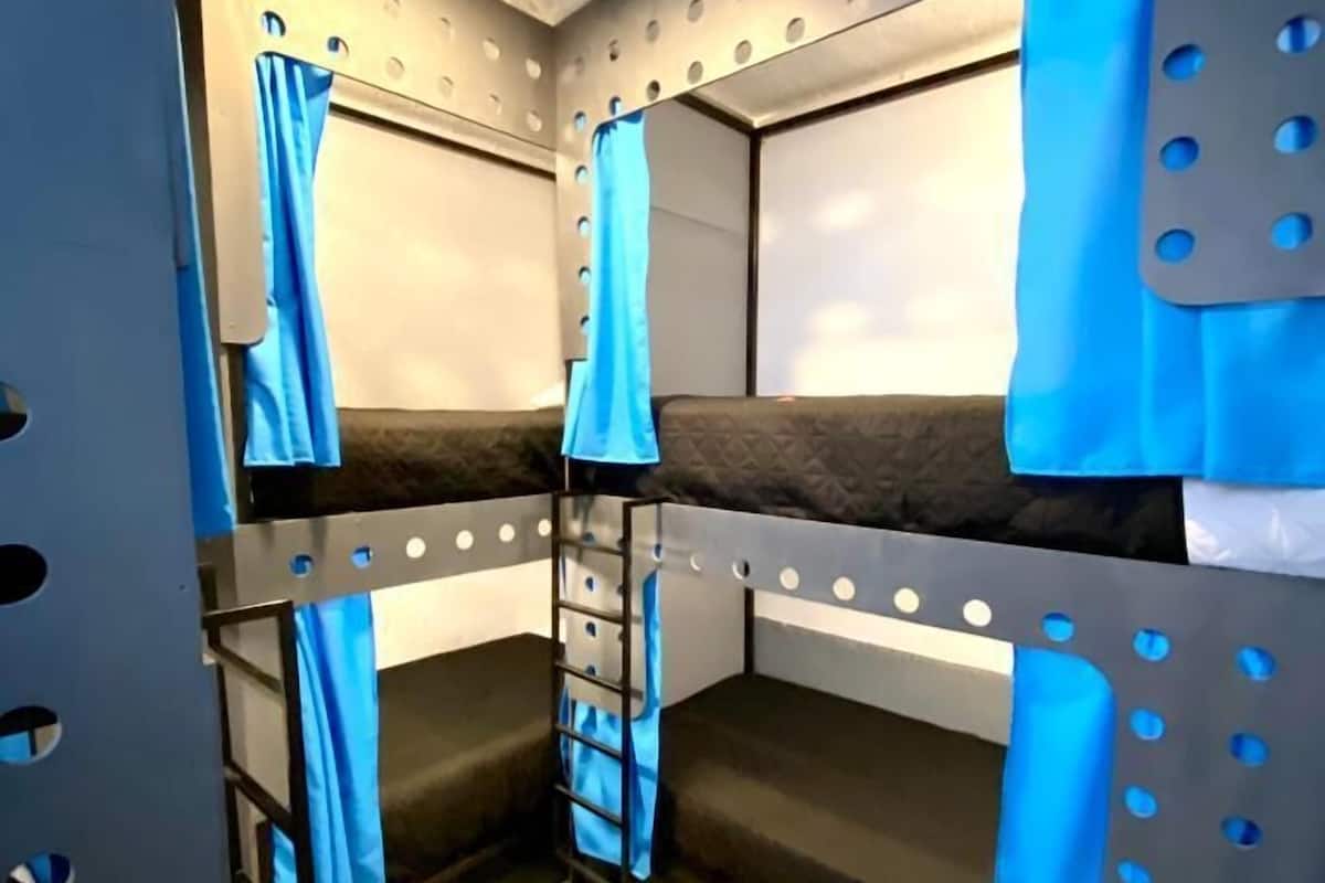 Ein Schlafraum mit Etagenbetten, einer Leiter, einem kleinen Fenster und einer Metallwand mit runden Aussparungen.