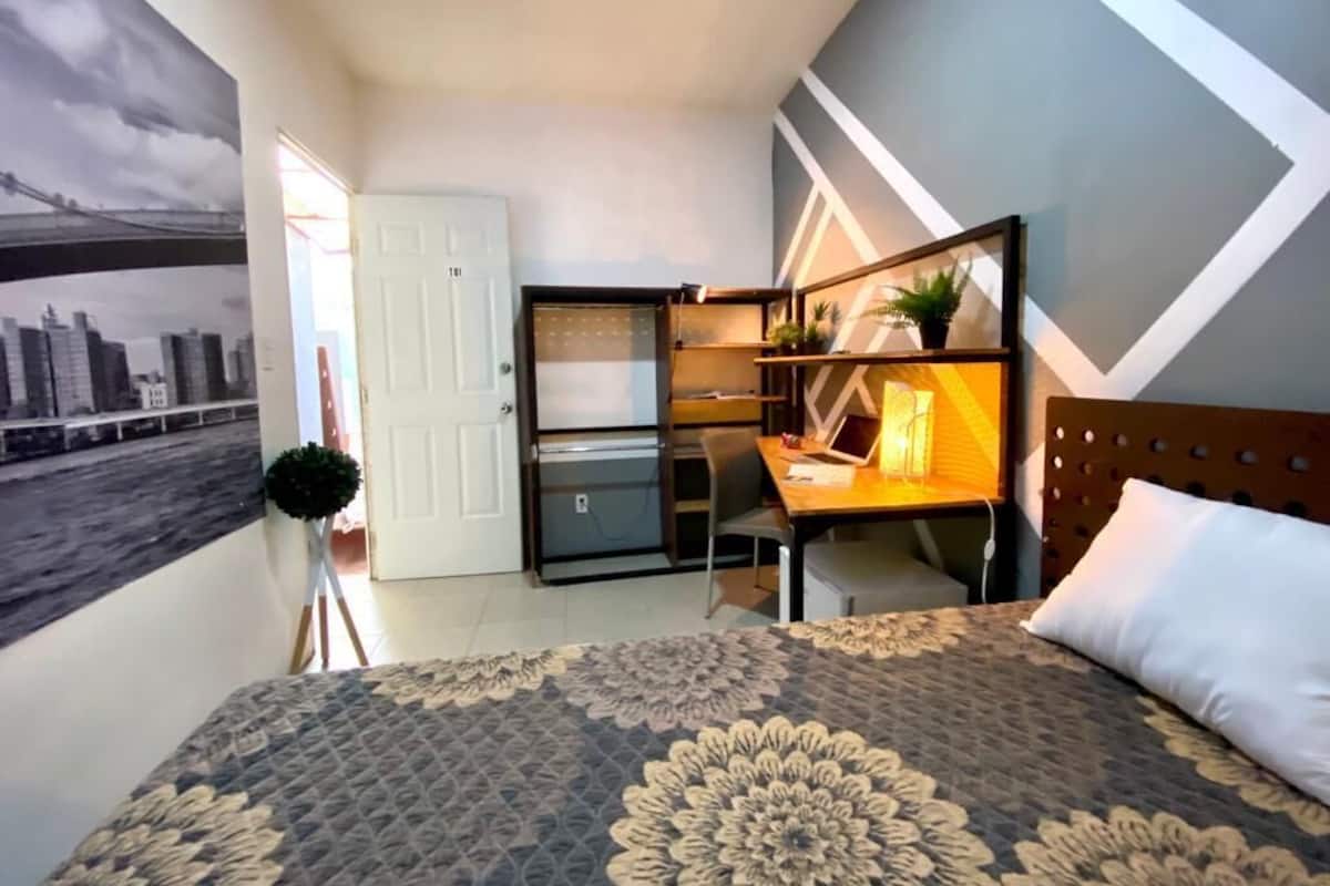 Ein Schlafzimmer mit Bett, Schreibtisch mit Stuhl, Kleiderschrank und einer Wand mit geometrischem Muster.