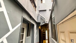Un pasillo estrecho con piso de baldosas, paredes grises con patrones geométricos blancos, y una puerta identificada con