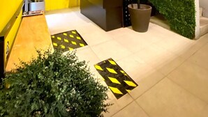 Una moderna zona de recepción con una pared de césped artificial verde, un muro geométrico amarillo y negro, y una escalera con piso a rayas amarillas y negras.