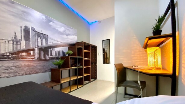 Una habitación de hotel moderna con una cama, un escritorio con una silla, una estantería y un mural grande con un paisaje urbano en la pared.