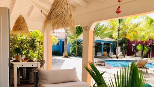 Un espace extérieur abrité, aménagé avec des meubles en osier, une piscine et des plantes tropicales.