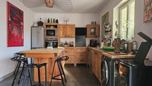 Eine moderne Küche mit Holzschränken, einer zentralen Kochinsel, Barhocker, einer Waschmaschine und einem großen Fenster.