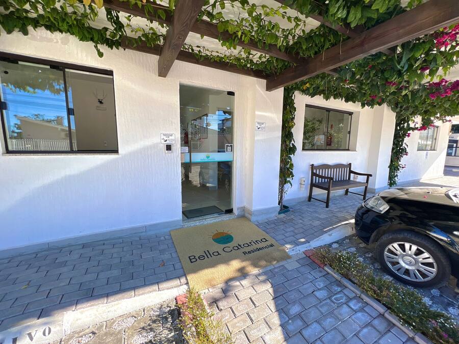 L'ingresso di un edificio residenziale con un tappetino, una panchina e un'auto parcheggiata davanti.