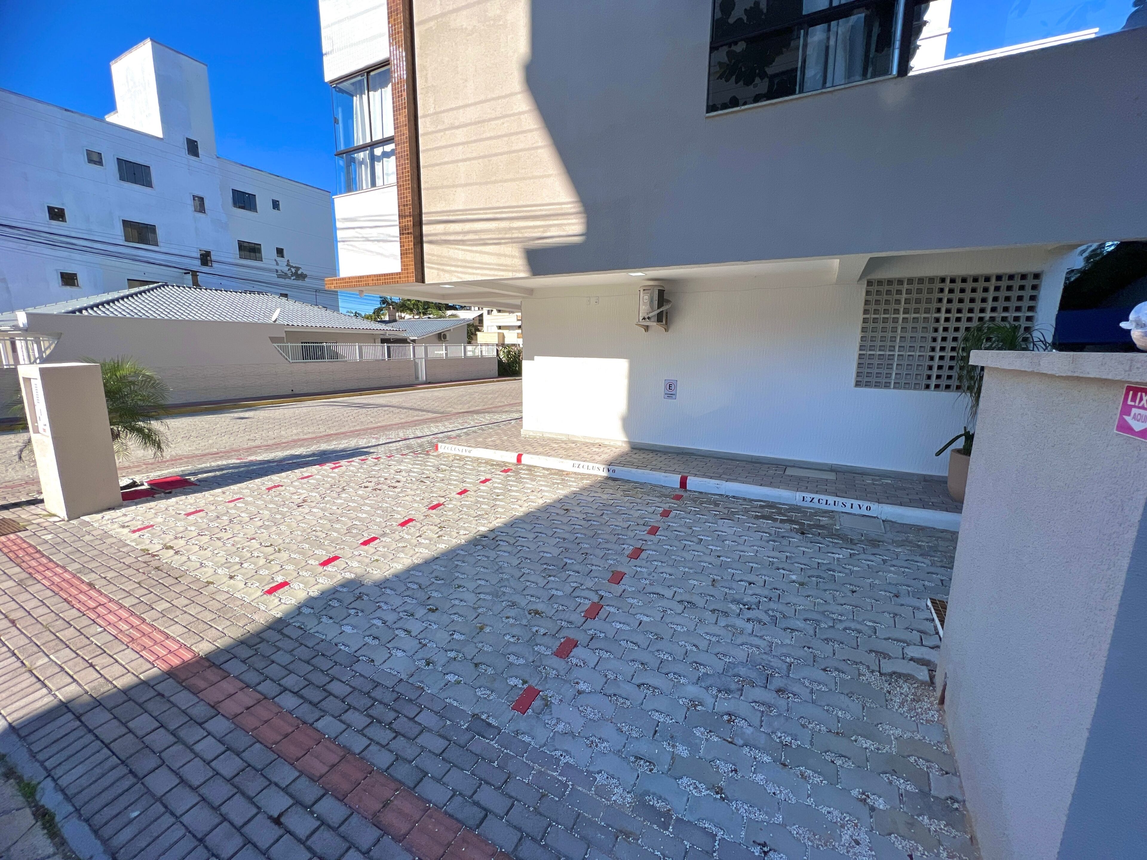 A paved courtyard with red and white markings, a white building with a window, and a clear blue sky.