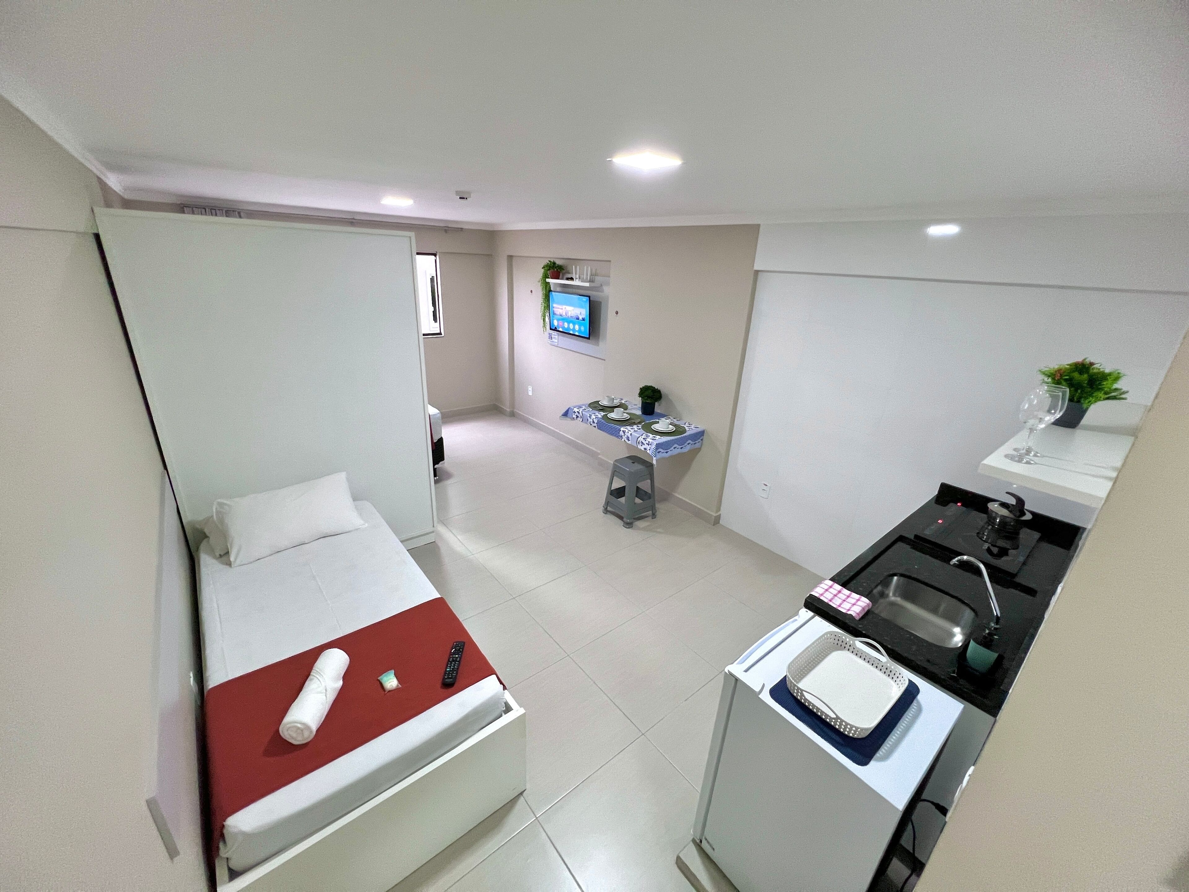 Una habitación de hotel pequeña con cama, kitchenette, una pequeña mesa de comedor y televisor.