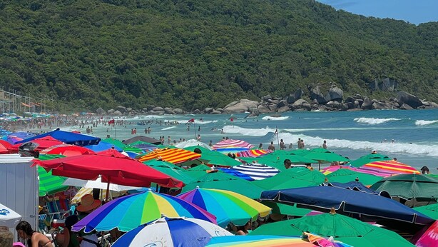 A beach with colorful umbrellas and people swimming in the water. - Bella Catarina Bombinhas (Bombinhas)