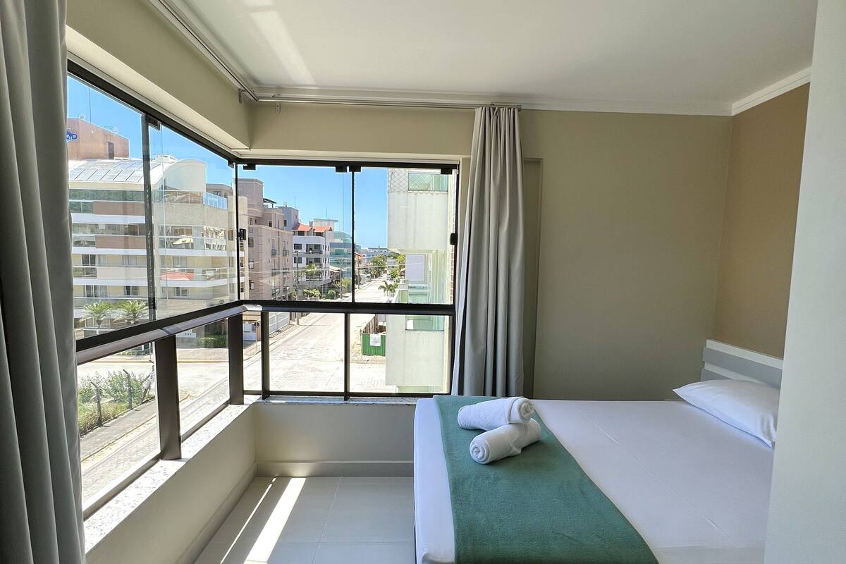 A hotel room with a balcony, a bed with a green bedspread, and a view of buildings and a street.