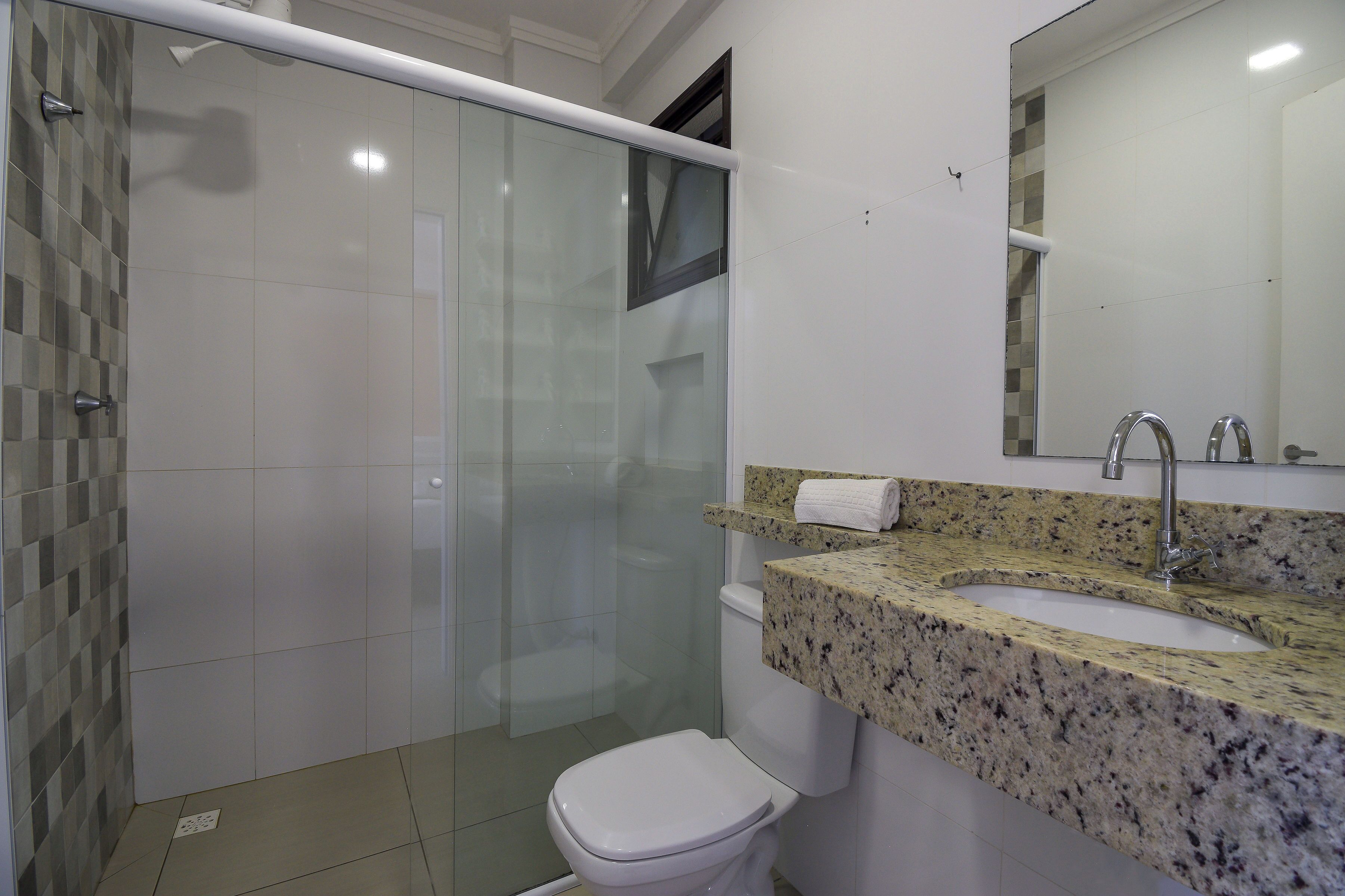 A bathroom with a glass shower enclosure, a white toilet, and a granite countertop sink with a mirror above.