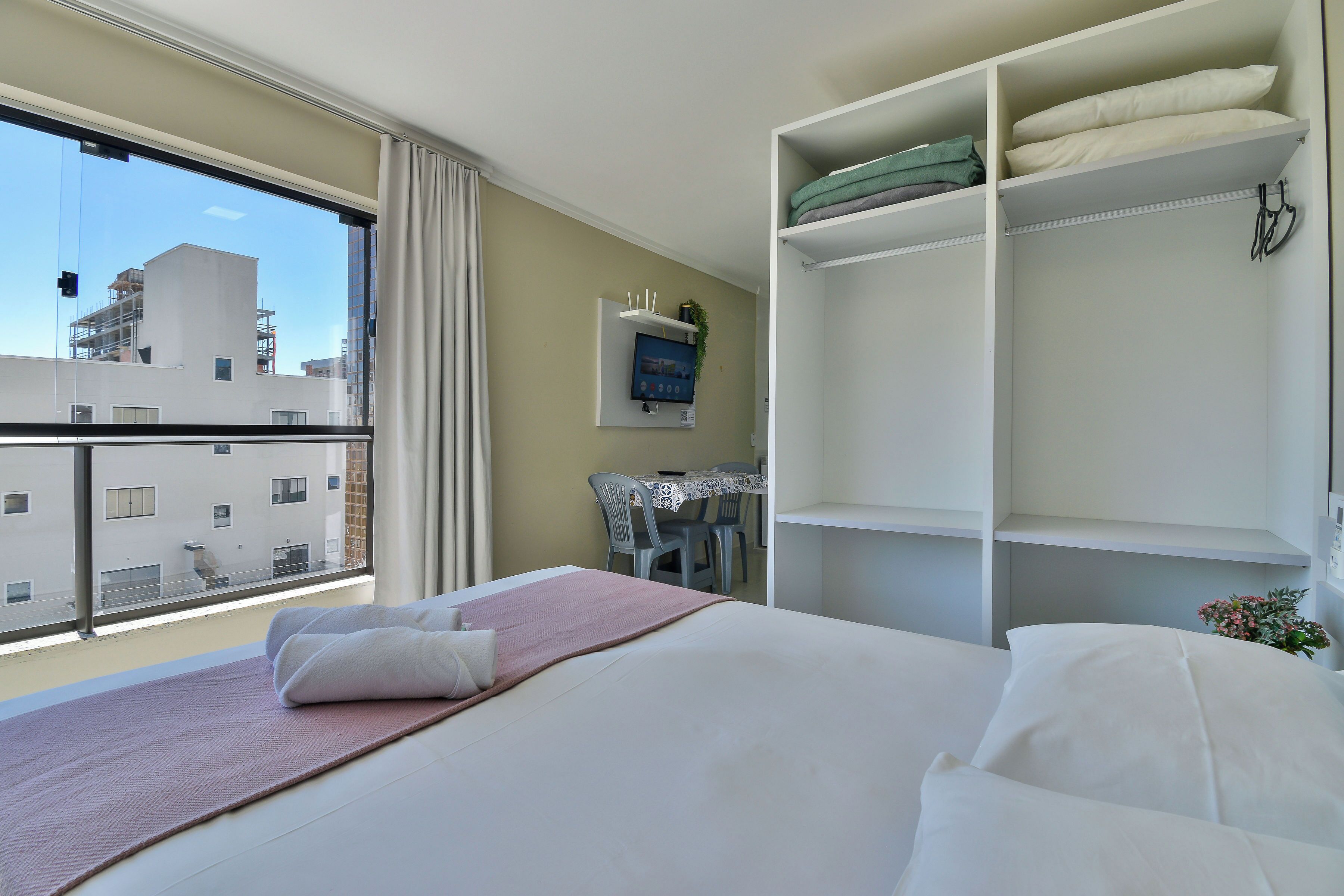 A hotel room with a bed, a desk, and a window with a view of buildings.