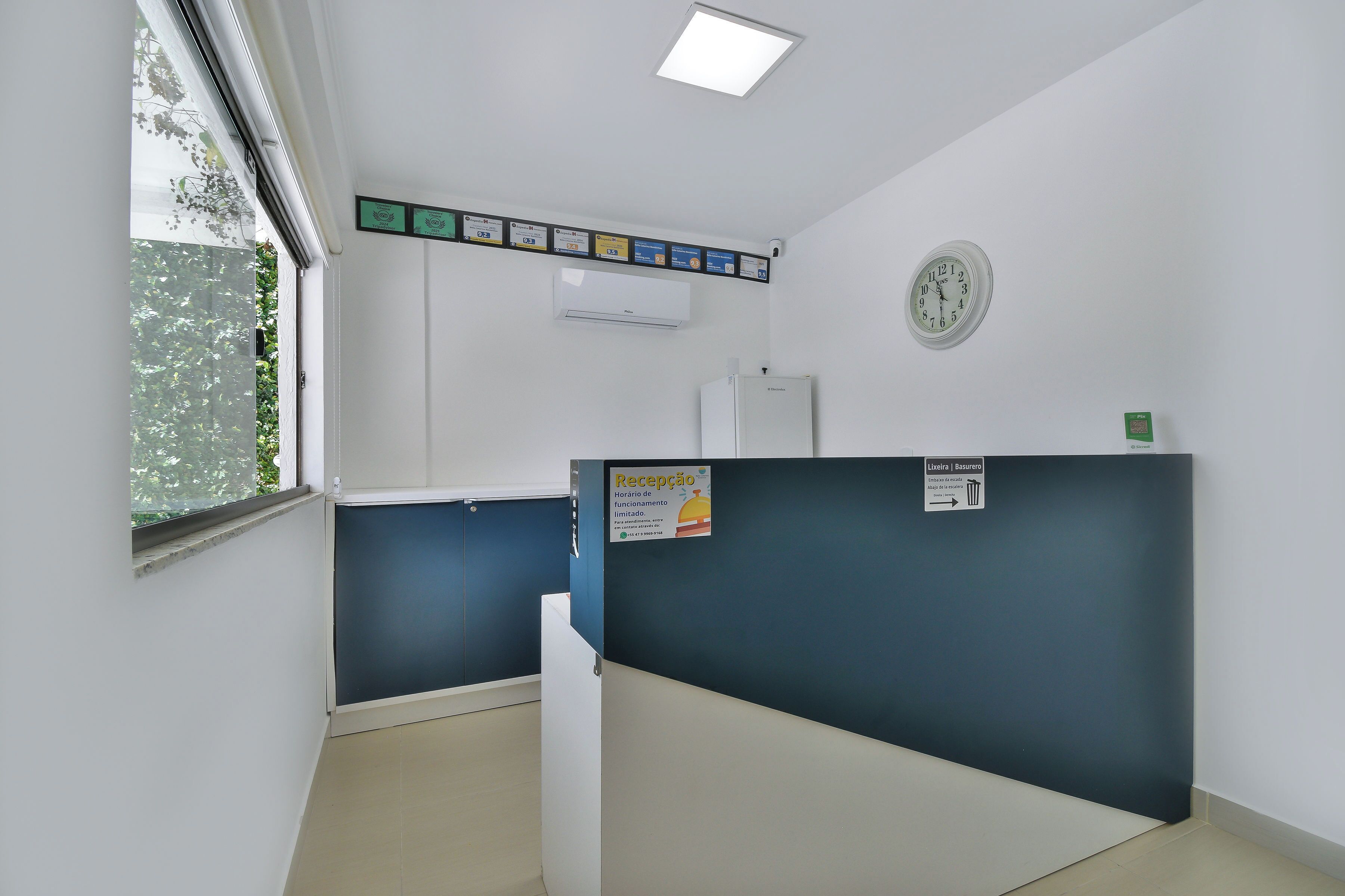A reception area with a clock, a window with a view of greenery, and a sign indicating reception hours.