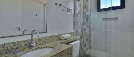 Un baño con lavamanos de encimera de granito, inodoro blanco y cabina de ducha con mampara de vidrio.