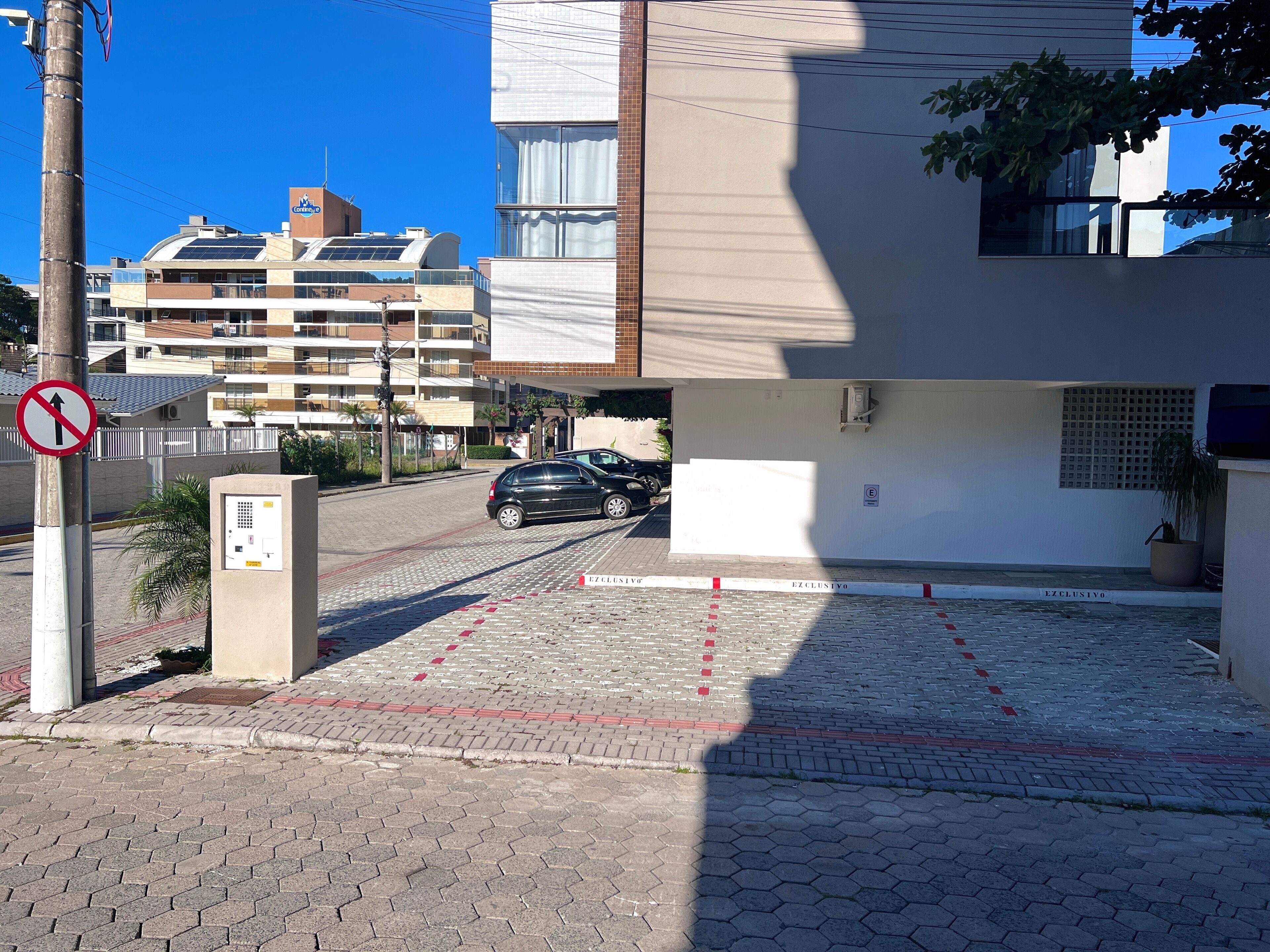 A parking area with a no parking sign, a car, and a building with a sign that reads "EXCLUSIVO."