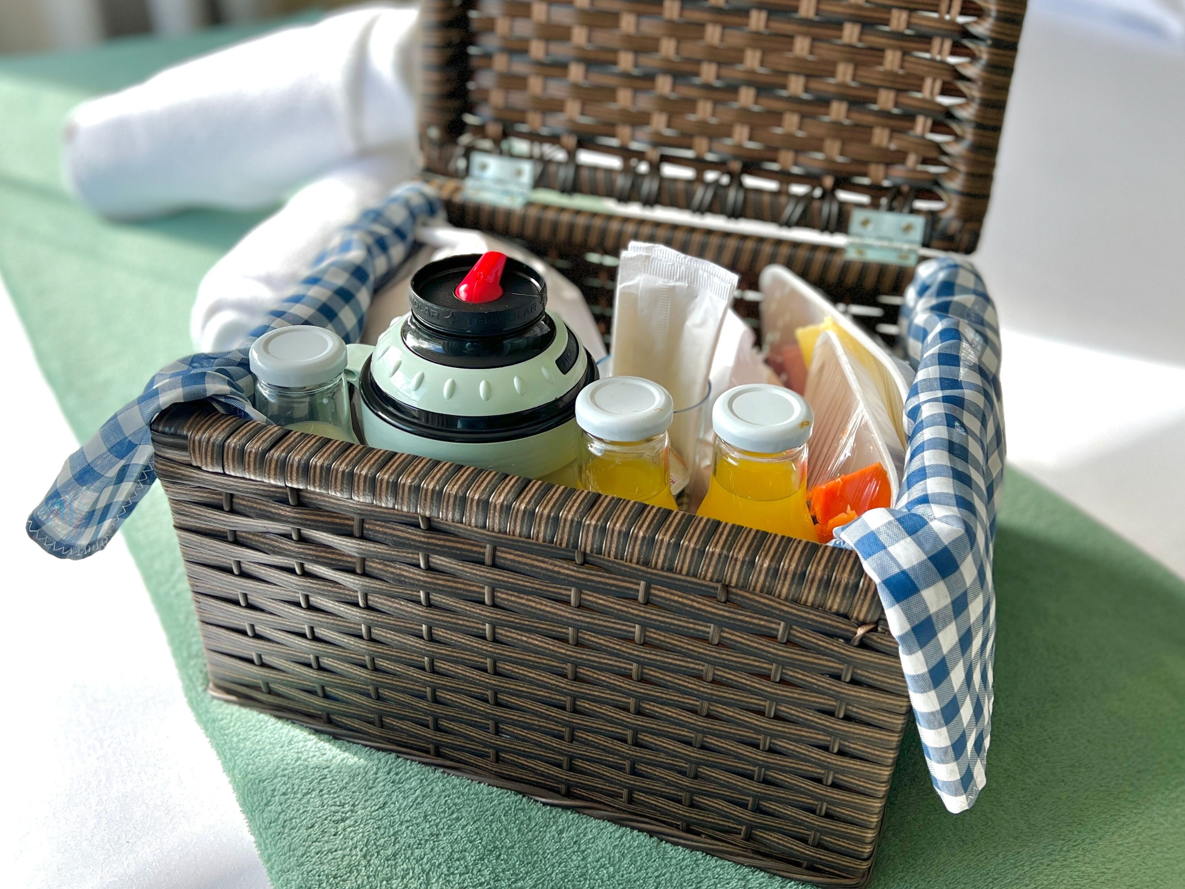 A wicker basket containing a portable water filter, two bottles of orange juice, a white bottle, and a blue and white checkered cloth.