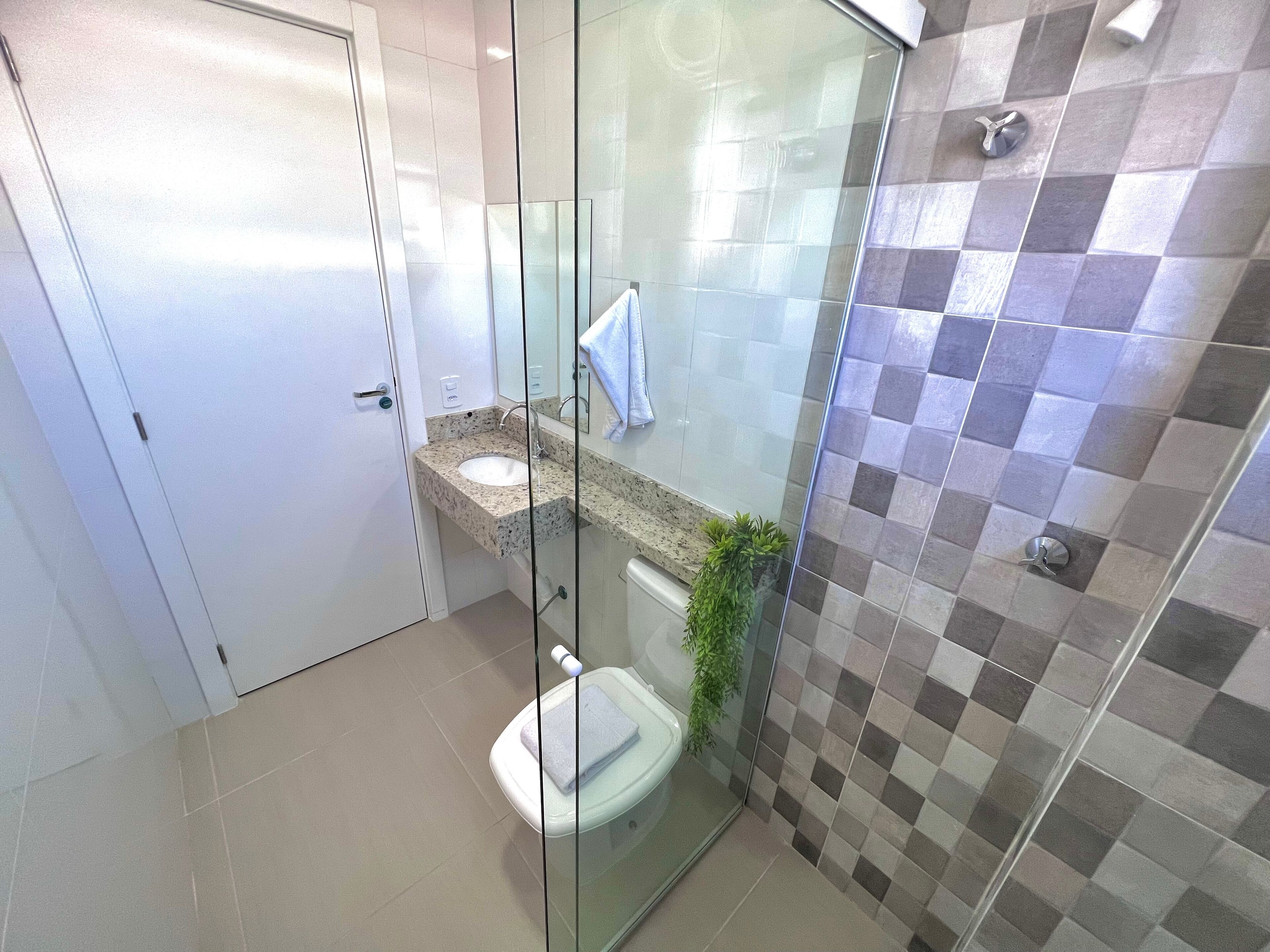 Et moderne badeværelse med en glasafskærmet bruseniche, en vask med bordplade i marmor og et toilet.
