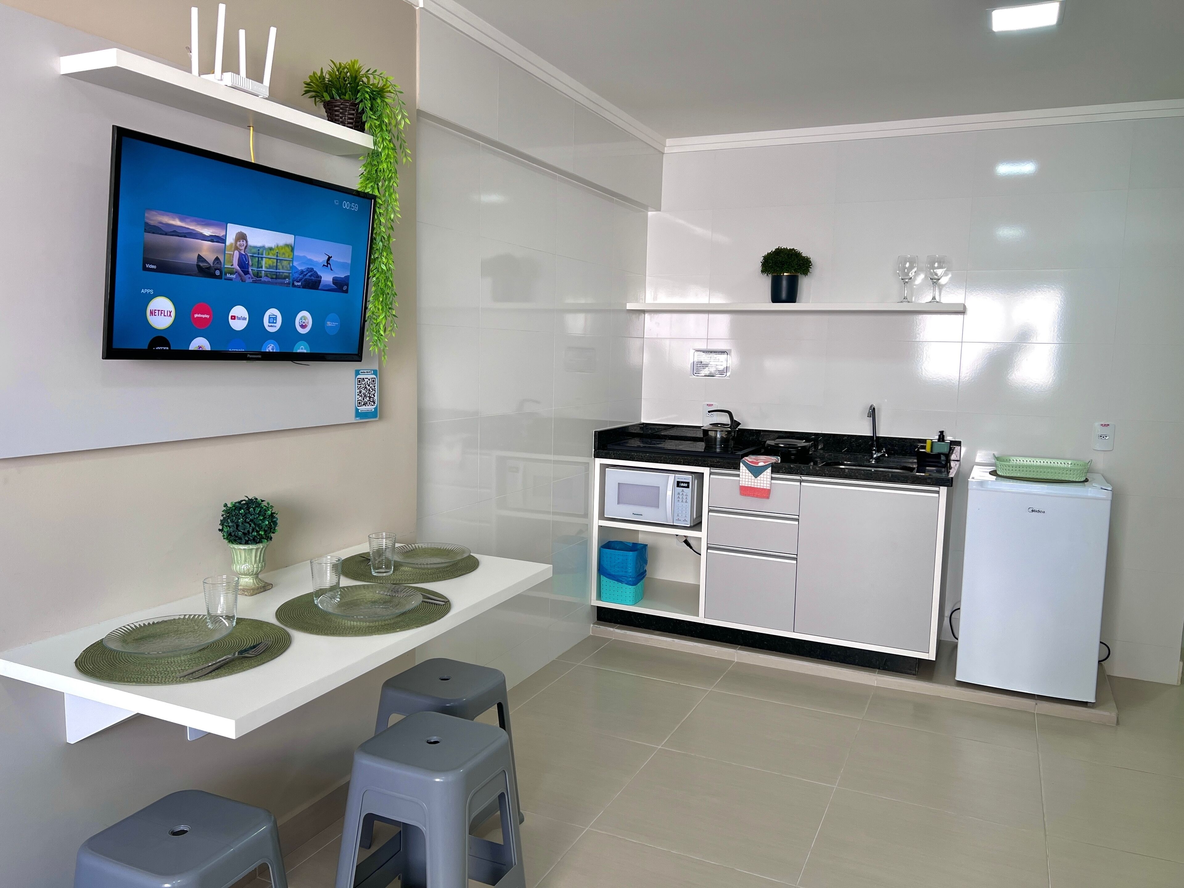 A modern kitchen with a flat-screen TV, white cabinets, a microwave, and a refrigerator.