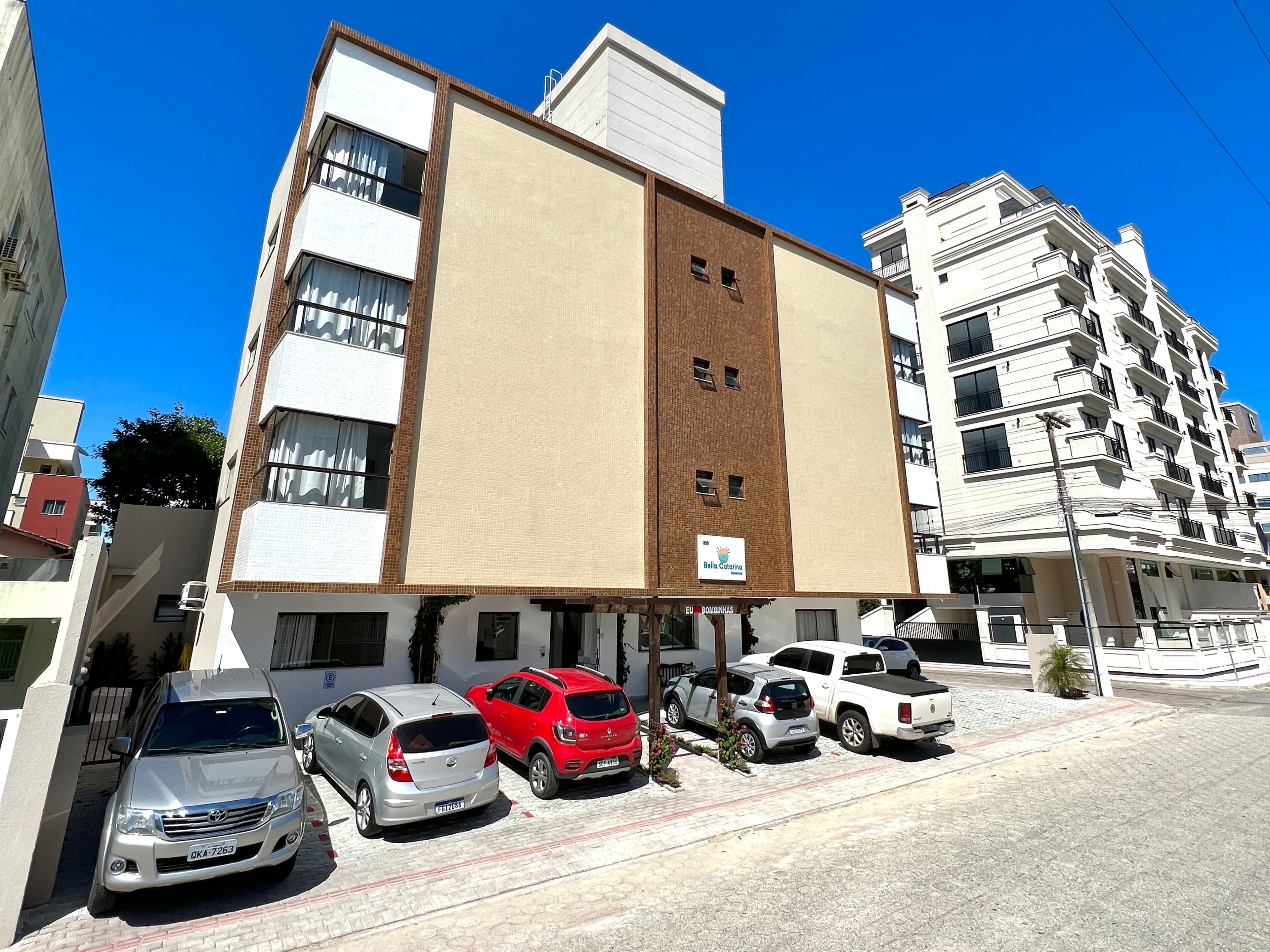 A multi-story building with a large billboard on the side, several parked cars, and a clear blue sky.