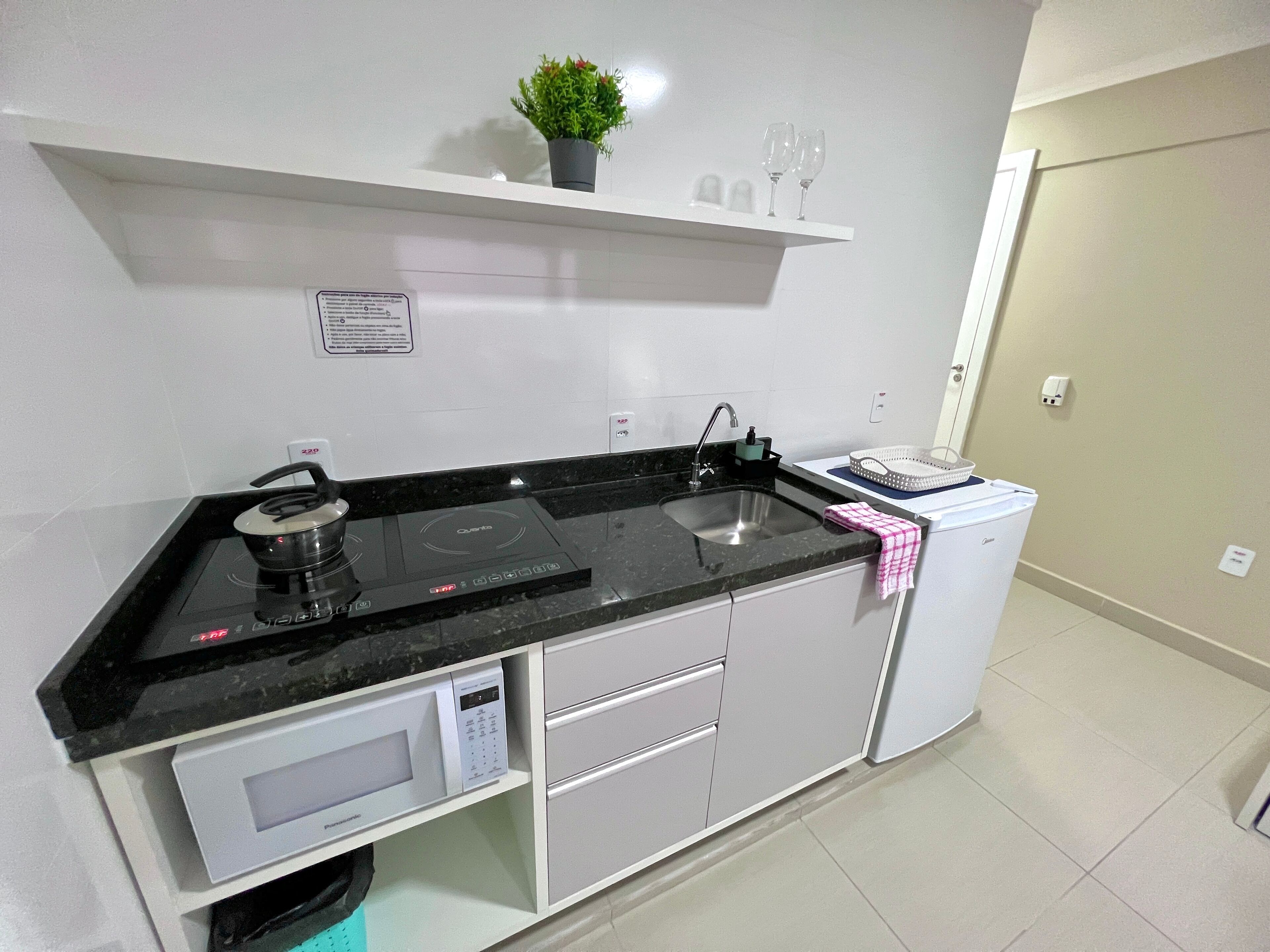 A modern kitchen with a black countertop, white cabinets, a microwave, a sink, and a small potted plant on a shelf.