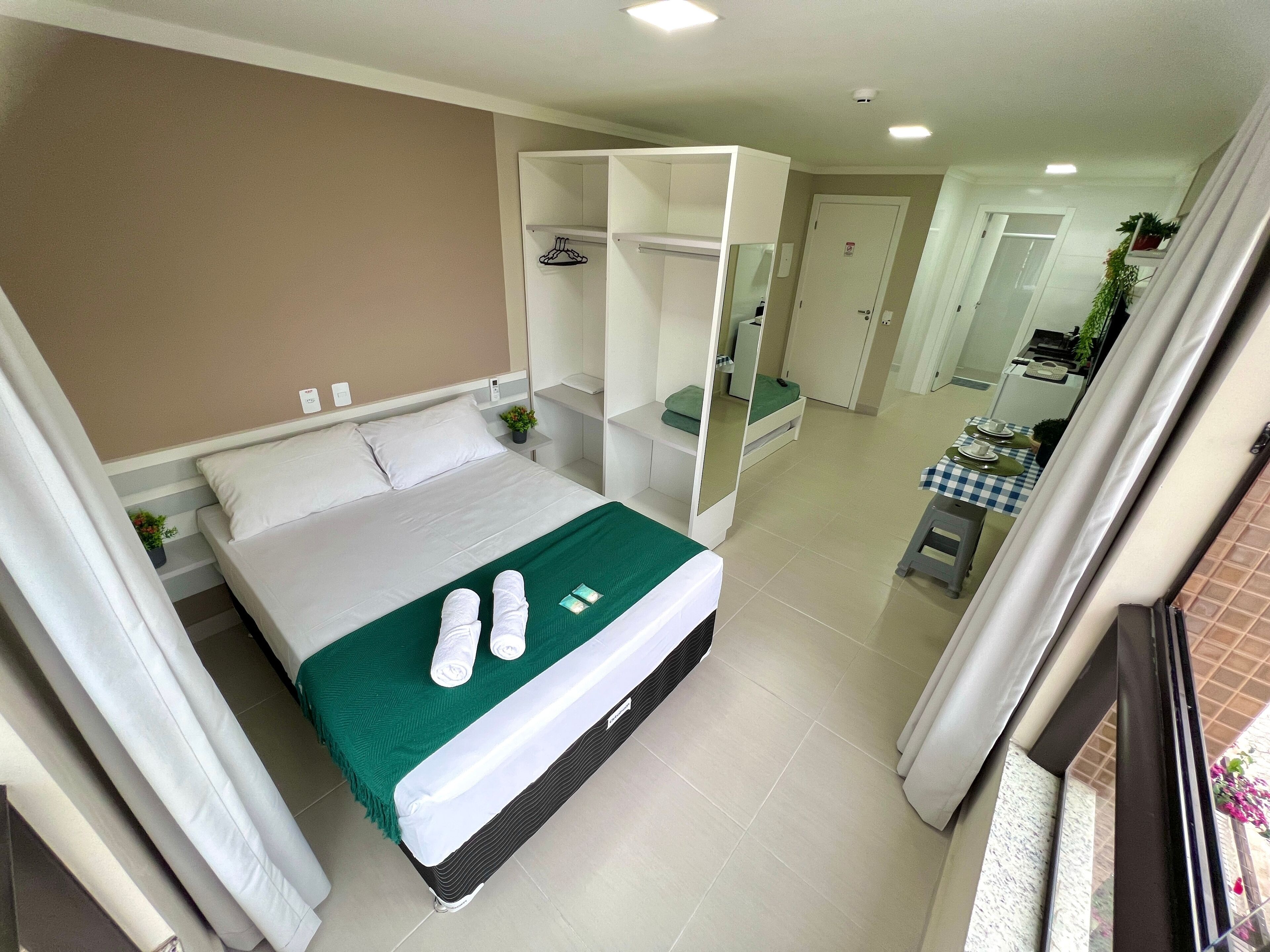 Una habitación de hotel con una cama, un armario, una mesita con mantel a cuadros y un baño visible a través de una puerta abierta.