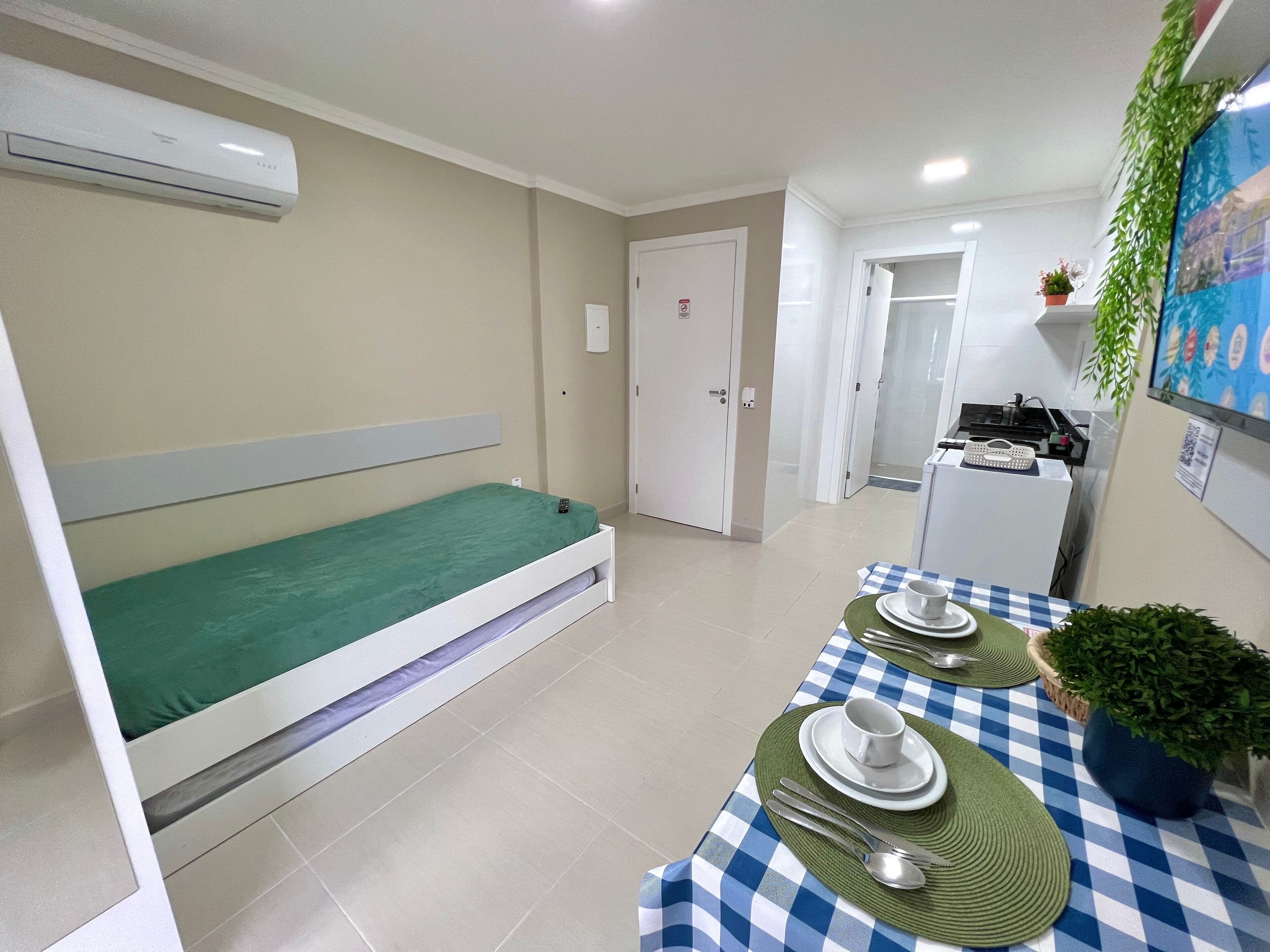 A hotel room with a bed, a dining table set with plates, a cup, and a spoon. There is a small kitchenette with a refrigerator and a microwave.