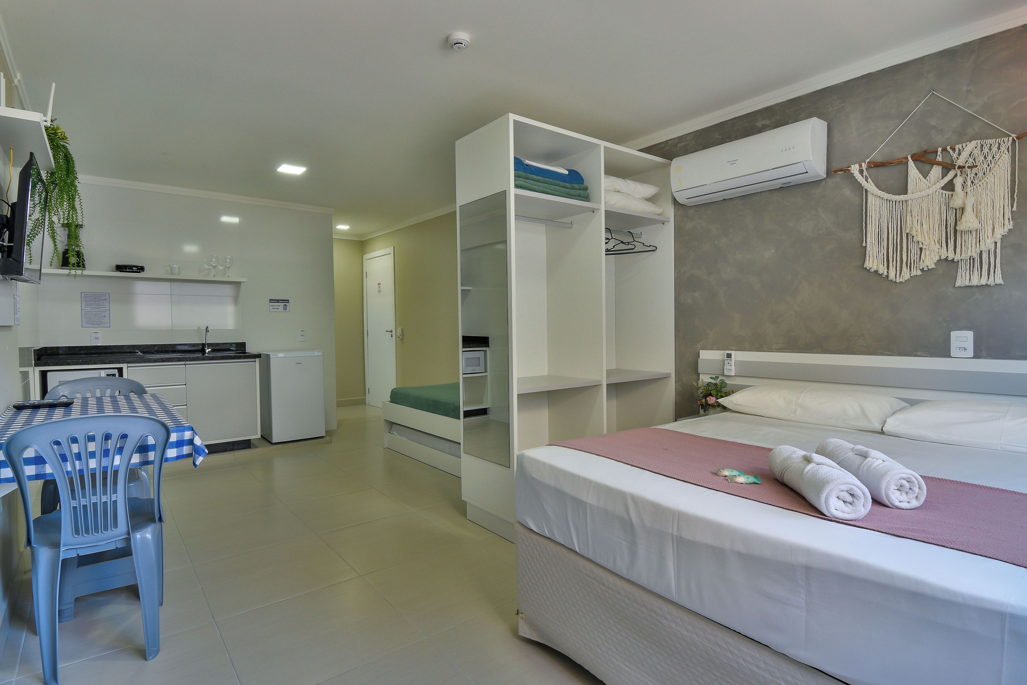 Een moderne hotelkamer met een bed, een bureau met stoel, een kitchenette en een inloopkast.