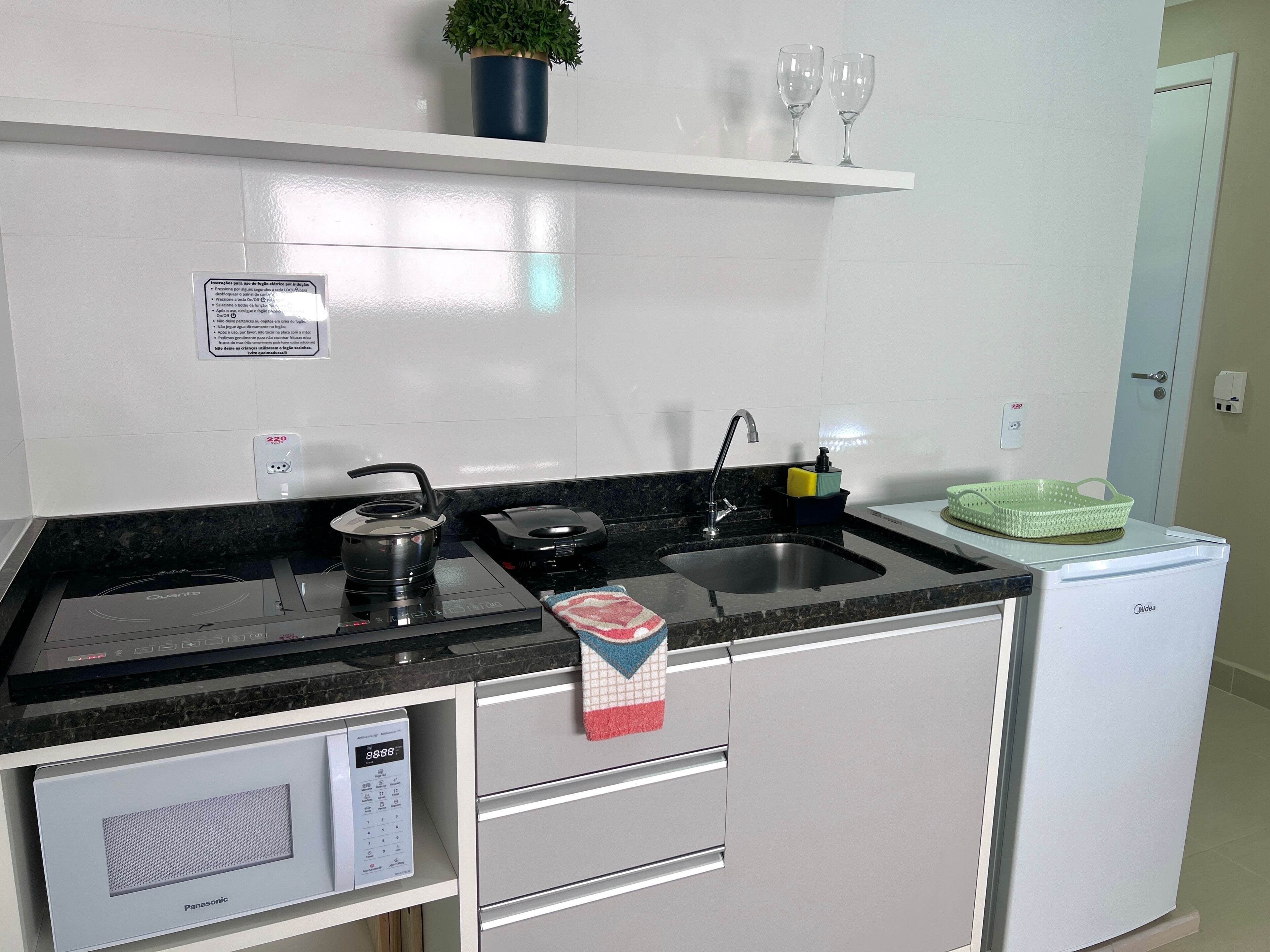 A modern kitchen with a built-in microwave, a kettle, a coffee maker, a sink, and a small refrigerator.