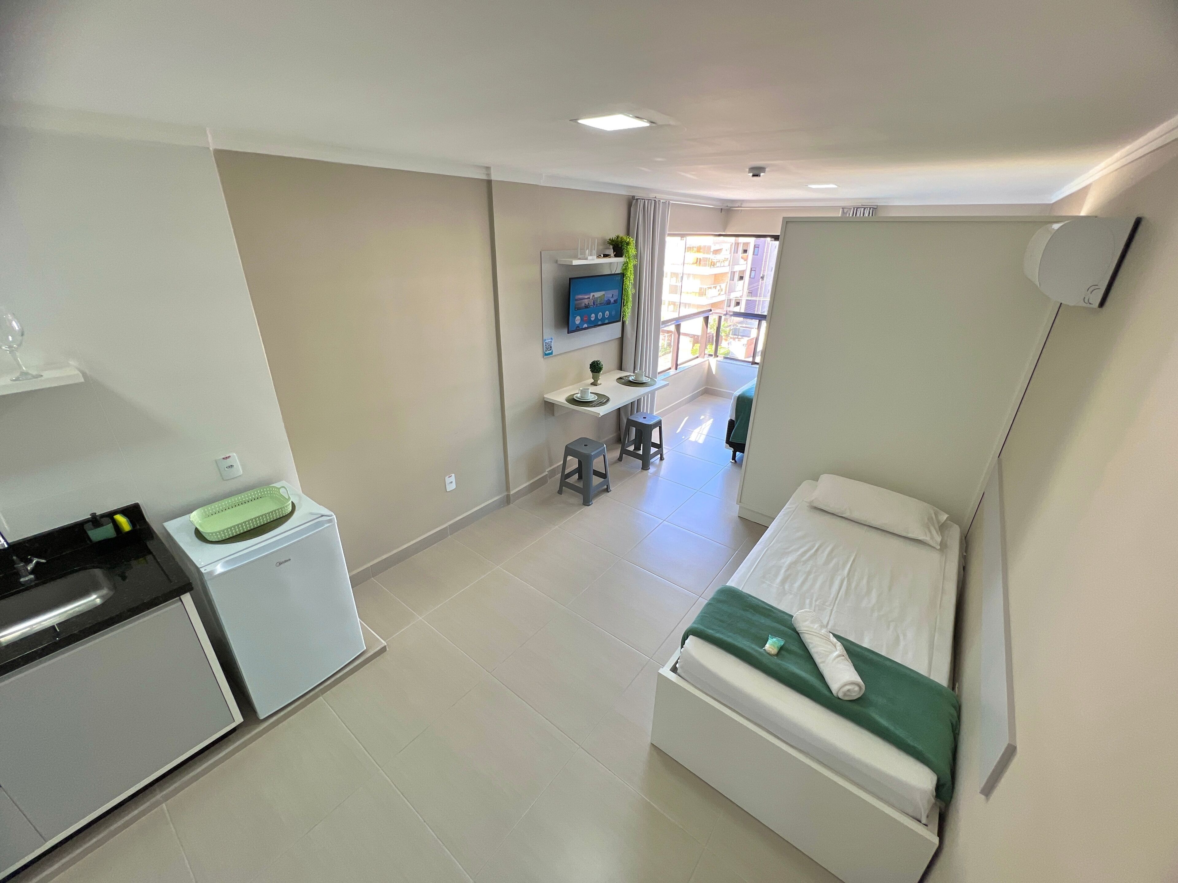 A small, clean room with a bed, a desk, and a kitchenette.
