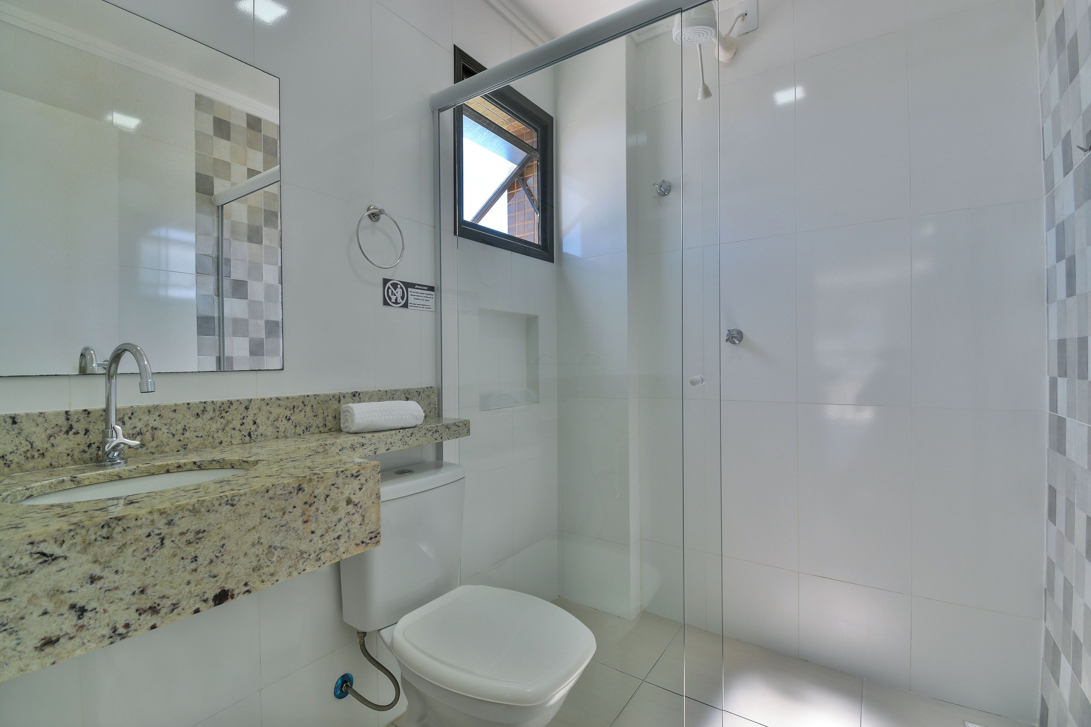 A bathroom with a granite countertop, a toilet, a glass shower enclosure, and a window.