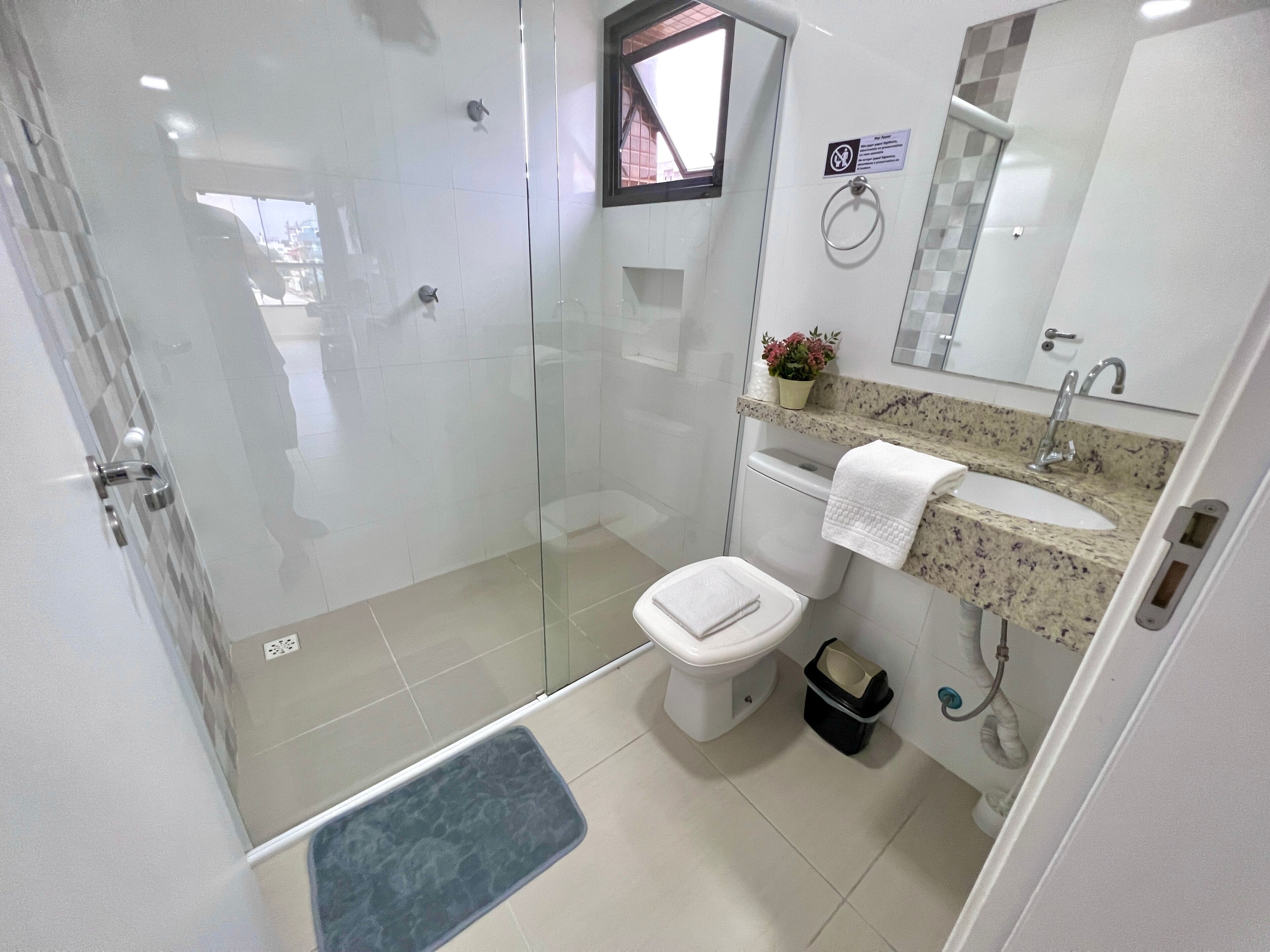 A modern bathroom with a glass-enclosed shower, a toilet, a sink with a marble countertop, and a mirror above the sink.