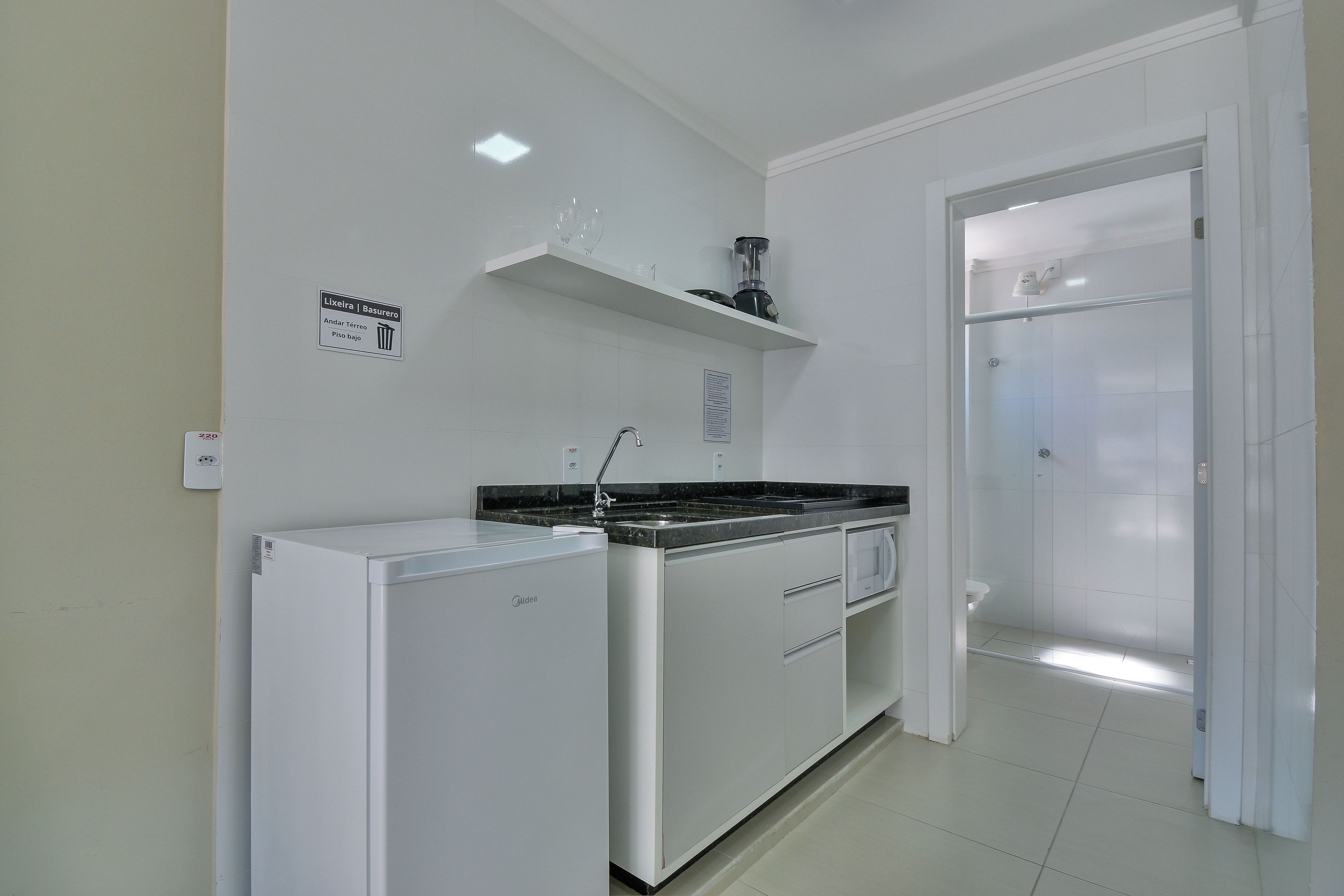 A compact kitchen with a refrigerator, stove, and a sink. There is a sign indicating the location of the trash bin.