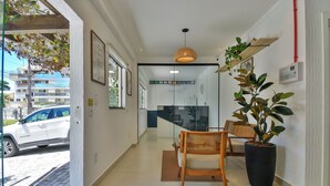 A hotel lobby with a reception desk, a large potted plant, a wicker chair, and a view of the street outside. - Bella Catarina Bombinhas (Bombinhas)