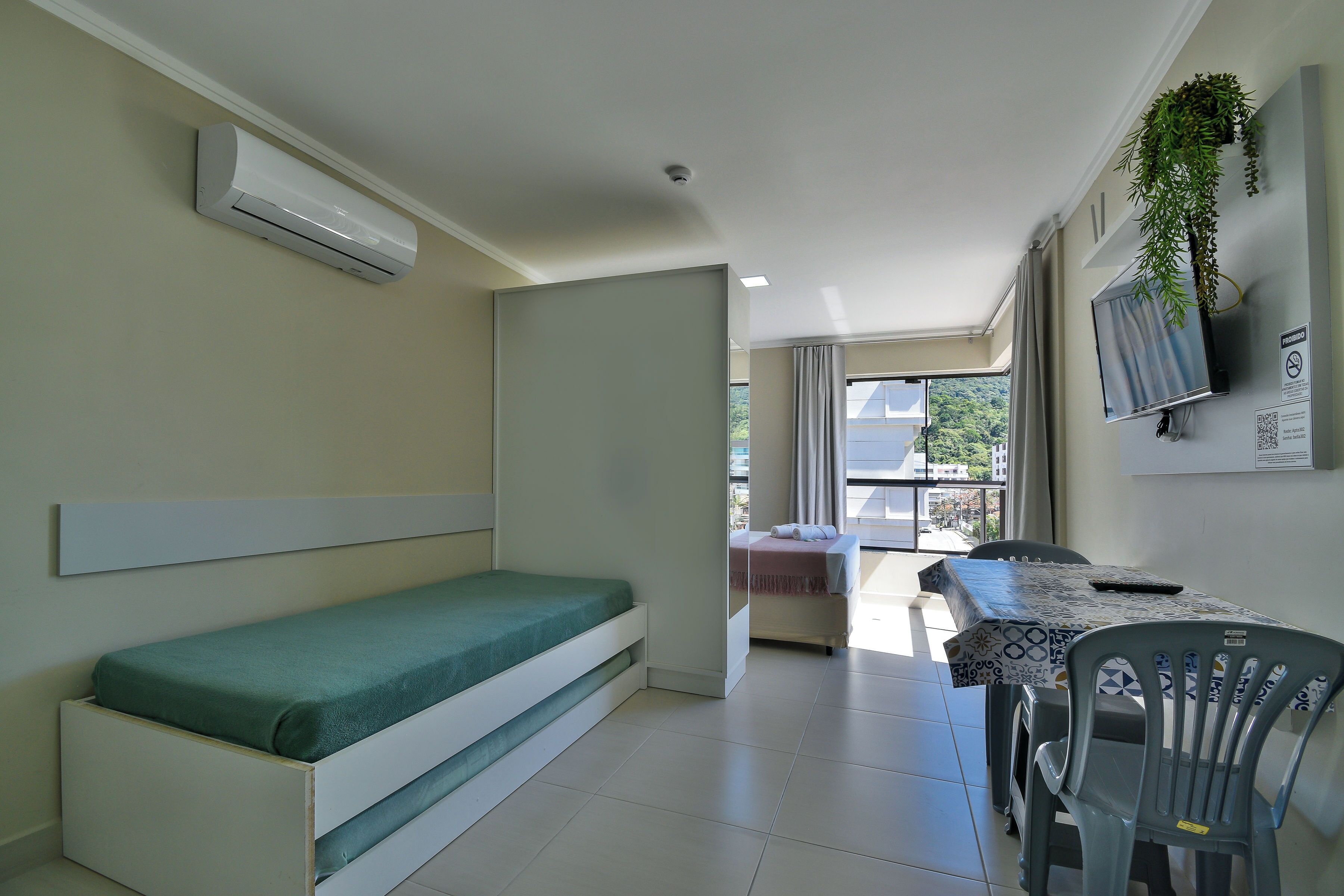 A compact room with a bed, a table, chairs, a TV, and an air conditioning unit.