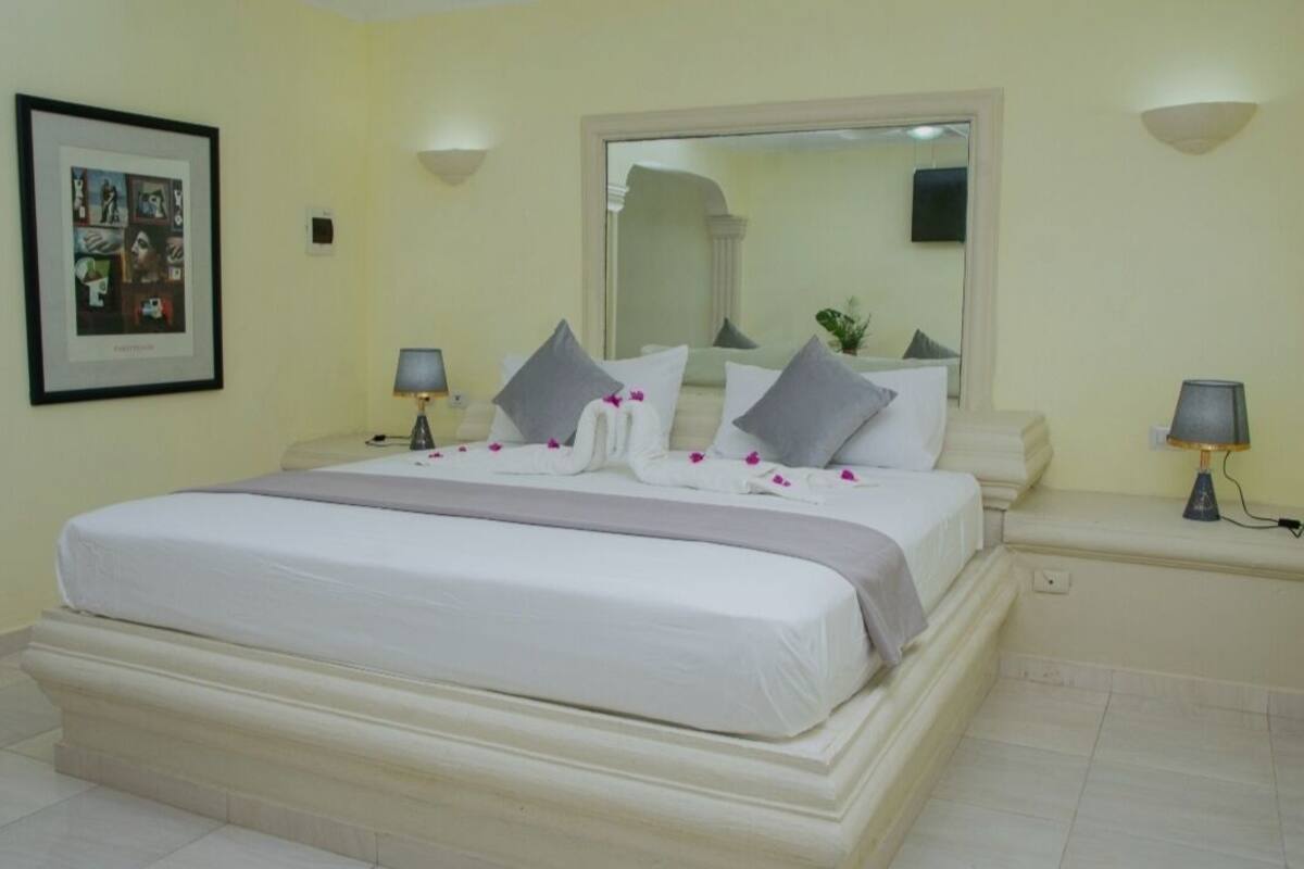 A hotel room with a large bed, two bedside tables with lamps, a framed picture on the wall, and a mirror above the bed.
