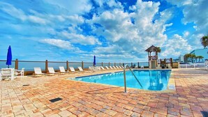 A pool area with lounge chairs and umbrellas, a pool, and a view of the ocean. - Sea Dip Resort Studios (Daytona Beach)