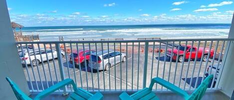 A balcony with two turquoise chairs overlooking a parking lot and the ocean.