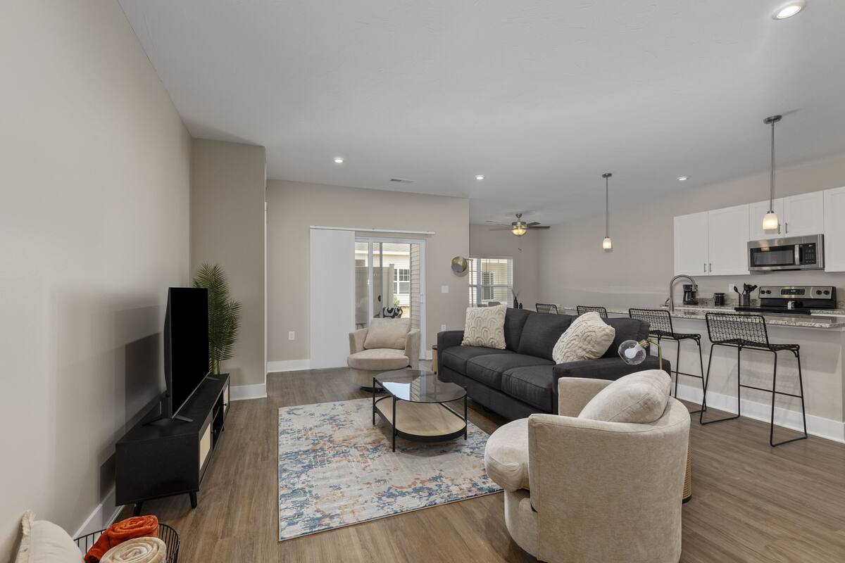 A modern living room with a flat-screen TV, a sofa, a coffee table, and a kitchen area with a microwave.