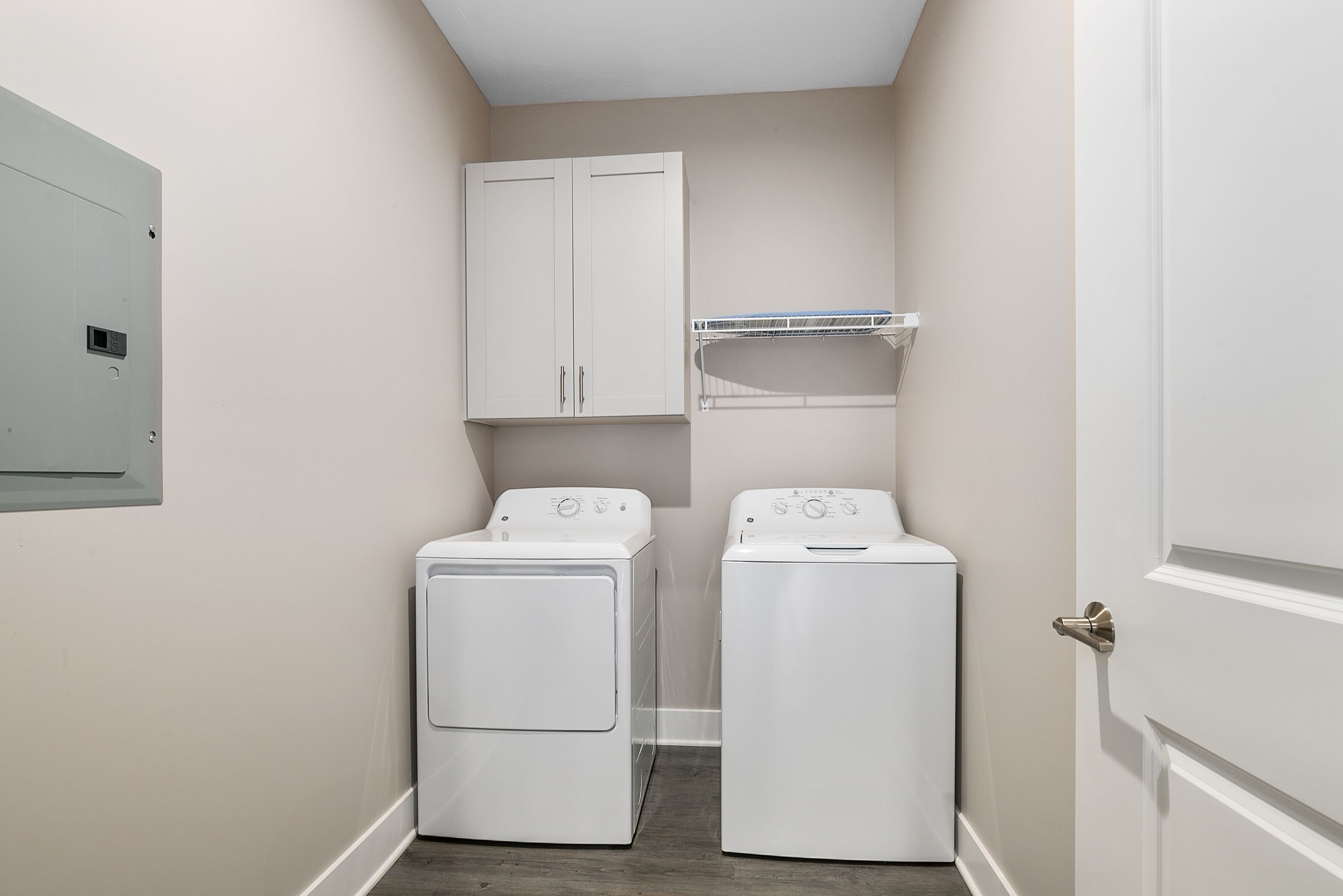 A laundry room with two white washing machines, a white cabinet, and a white shelf unit.