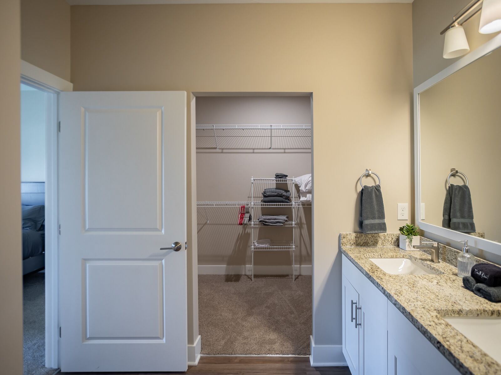 A modern bathroom with a large mirror, a sink, and a walk-in closet with shelves.