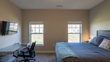 A bedroom with a bed, a desk with a chair, a TV, and two windows.