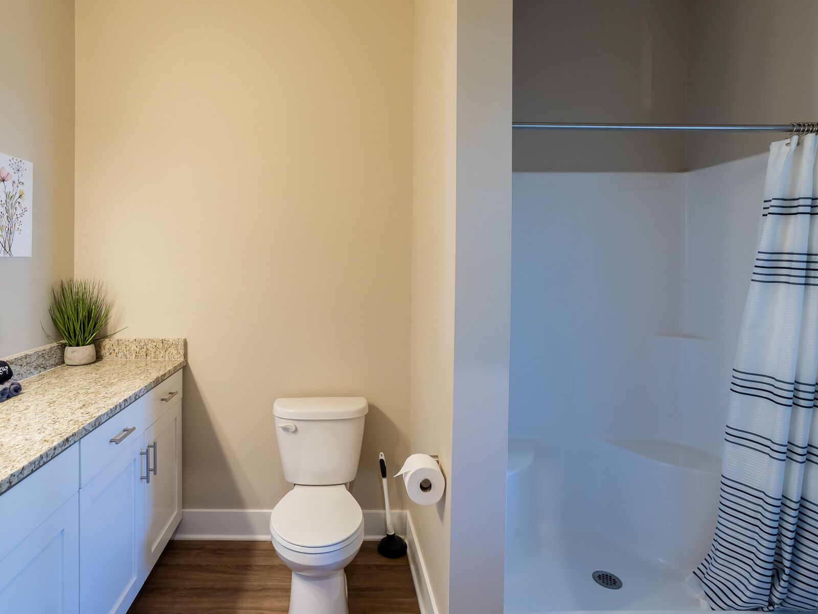 A bathroom with a toilet, a shower, and a sink with a plant.