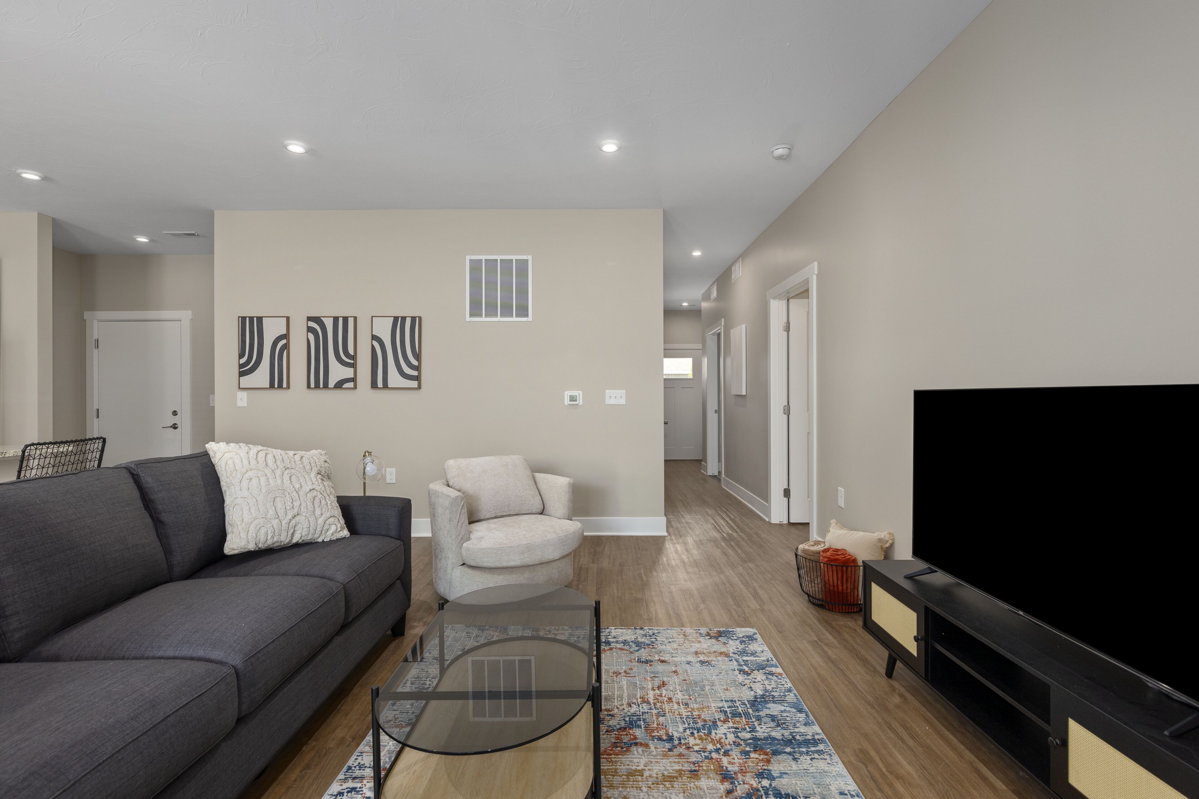 A modern living room with a gray sofa, a white armchair, a glass coffee table, and a flat-screen TV.
