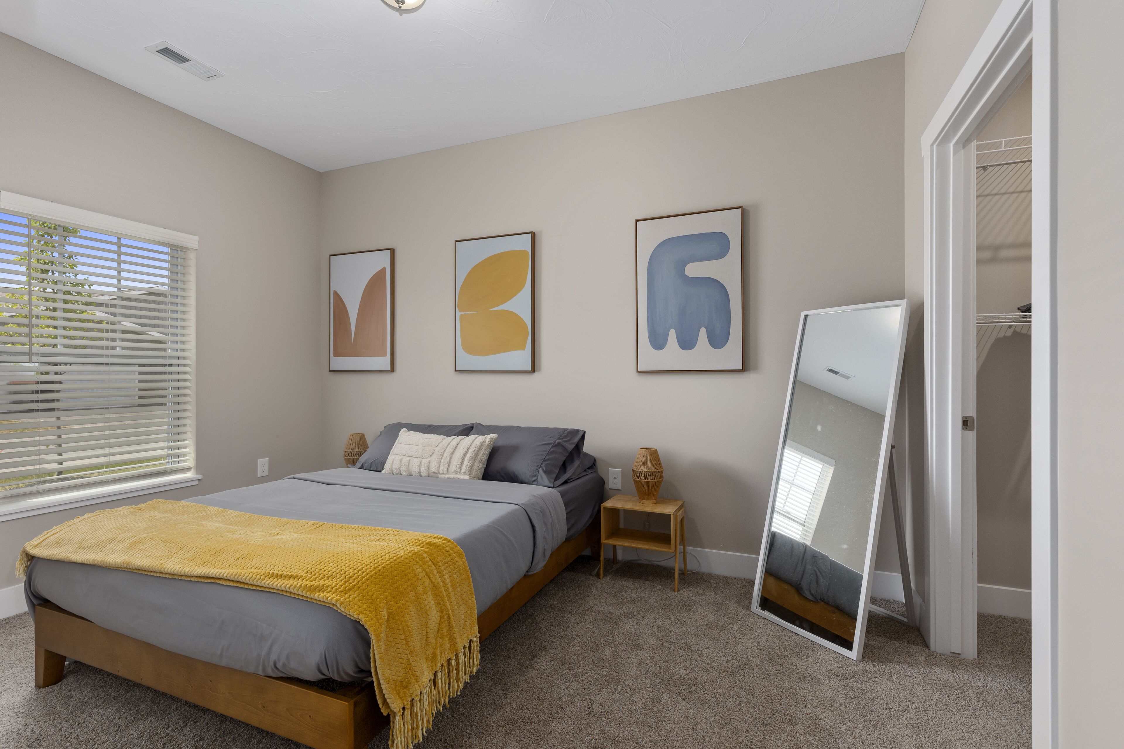 A bedroom with a bed, bedside tables, a mirror, and artwork on the wall.